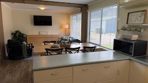 Una cocina compacta con comedor, un televisor de pantalla plana y un ventanal con persianas.