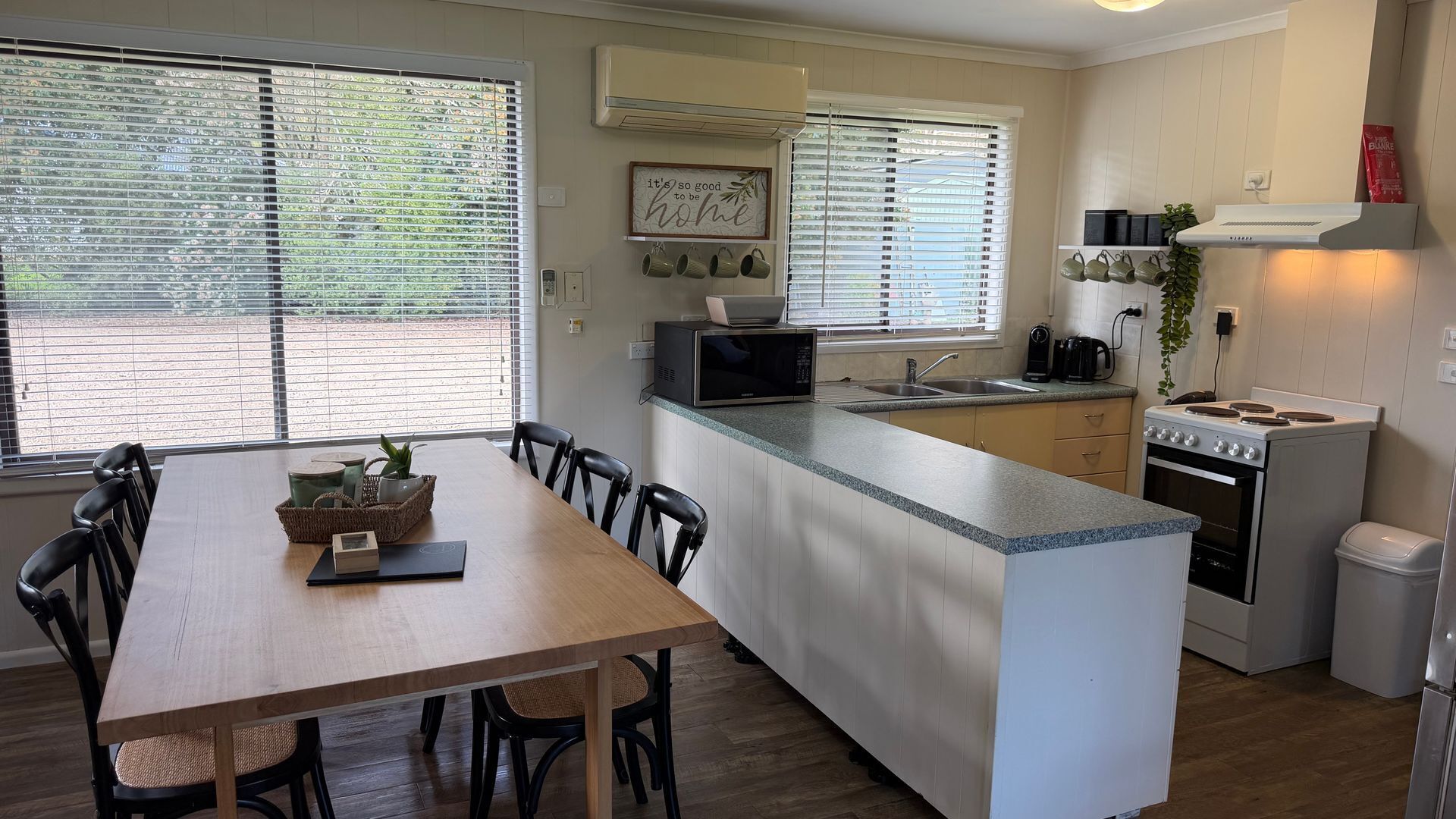 A compact kitchen with a central island, a dining area with a wooden table and chairs, and a view through the windows.