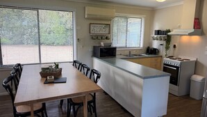 Une cuisine compacte avec un îlot central, un coin repas avec une table et des chaises en bois, et une vue par les fenêtres.