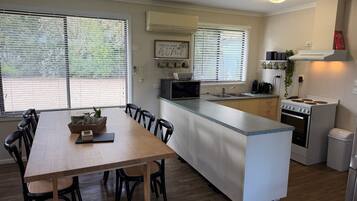 A compact kitchen with a central island, a dining area with a wooden table and chairs, and a view through the windows.