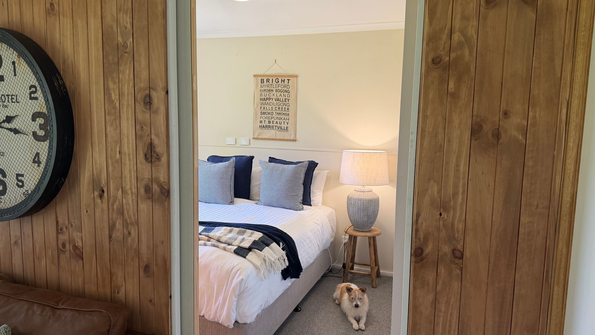 A bedroom with a bed, pillows, a lamp, and a dog.