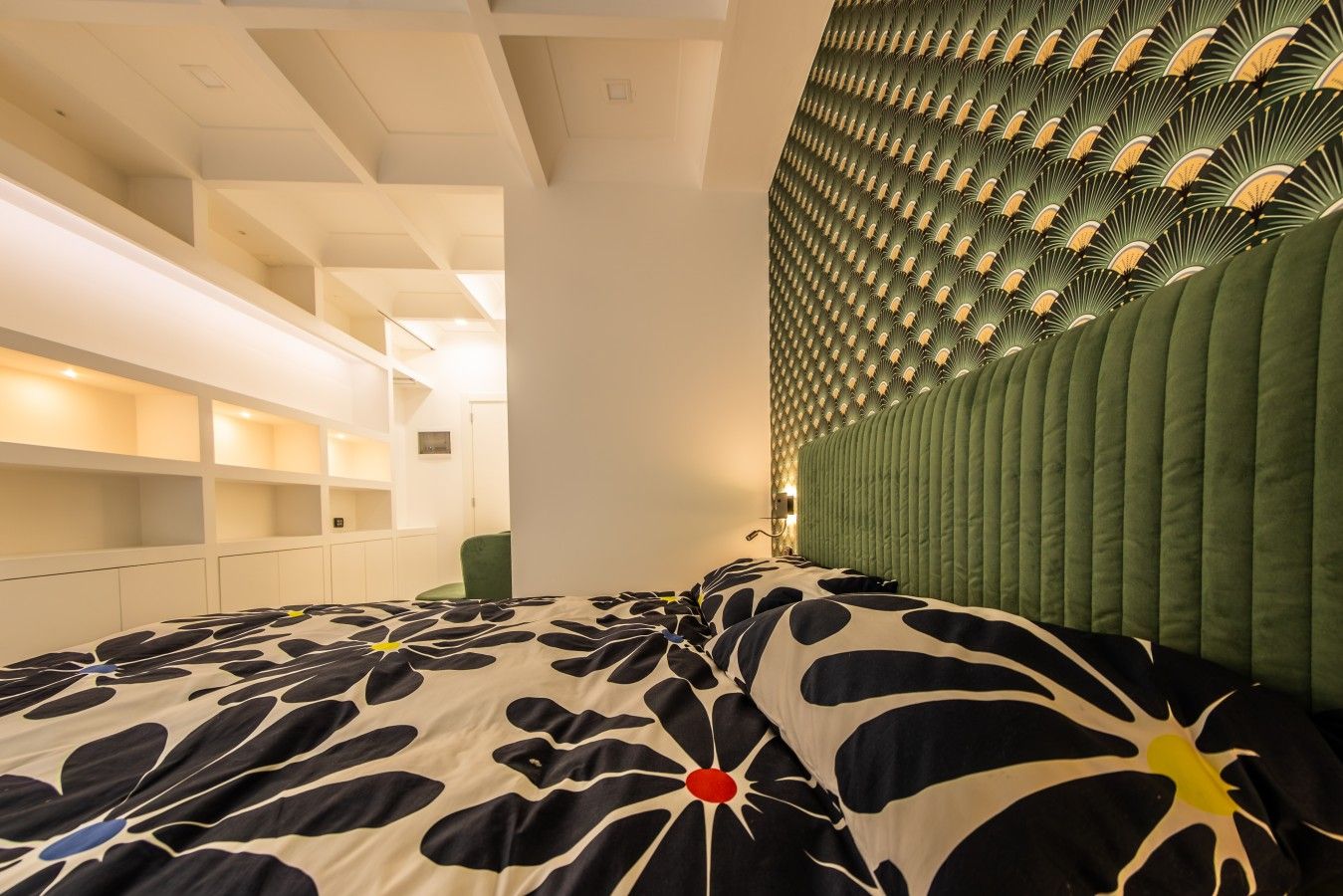 A modern bedroom with a patterned bedspread, built-in shelving, and a unique green headboard.