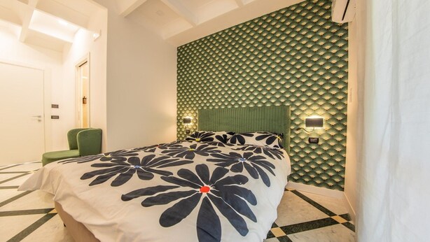 Ein Hotelzimmer mit einem Bett, einem grünen Polsterstuhl, einer Wand mit Muster und einer Decke mit geometrischem Design.