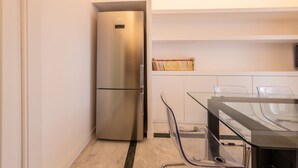 Eine kleine Küche mit einem Edelstahlkühlschrank, einem Glastisch und einem weißen Schrank mit einem gewebten Korb.