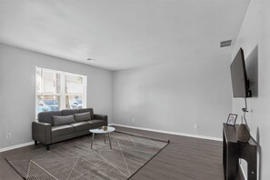 A modern living room with a grey sofa, a coffee table, and a TV mounted on the wall. - Comfortable Townhome with Modern Interiors (Indianapolis)