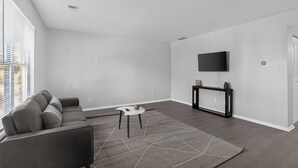 A modern living room with a grey sofa, a coffee table, a TV mounted on the wall, and a patterned rug. - Comfortable Townhome with Modern Interiors (Indianapolis)
