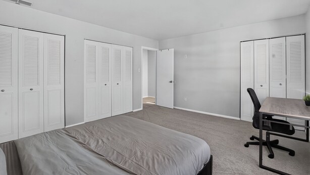 A bedroom with a bed, a desk, and a chair. There are two sets of white closets with louvered doors. - Comfortable Townhome with Modern Interiors (Indianapolis)