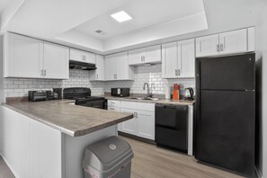 A modern kitchen with white cabinets, a black refrigerator, a microwave, a stove, and a sink. - Comfortable Townhome with Modern Interiors (Indianapolis)