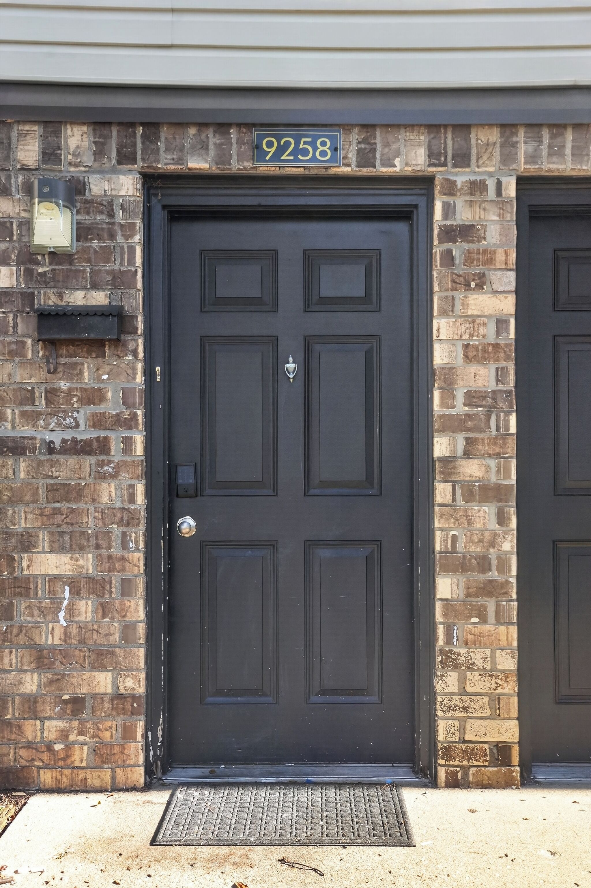 A black door with a number plate reading 9258, a mailbox, and a doormat.