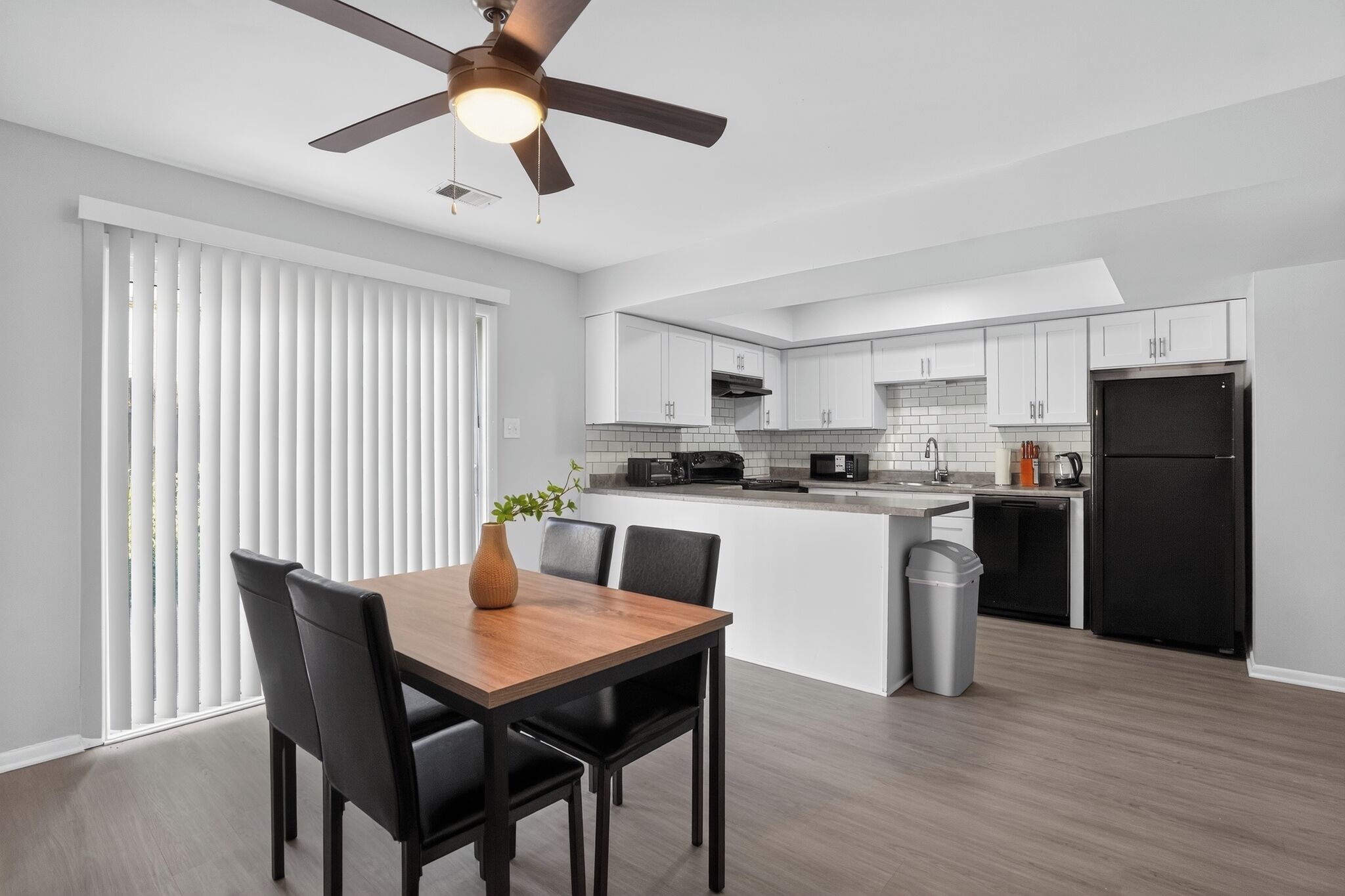 A modern kitchen with white cabinets, a black refrigerator, and a dining area with a wooden table and chairs.