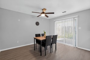 A dining area with a table and chairs, a ceiling fan, a clock, and a view through a window with blinds. - Comfortable Townhome with Modern Interiors (Indianapolis)