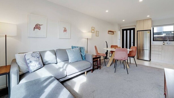 A modern living room with a sofa, chairs, a dining table, and a kitchen area with a refrigerator.