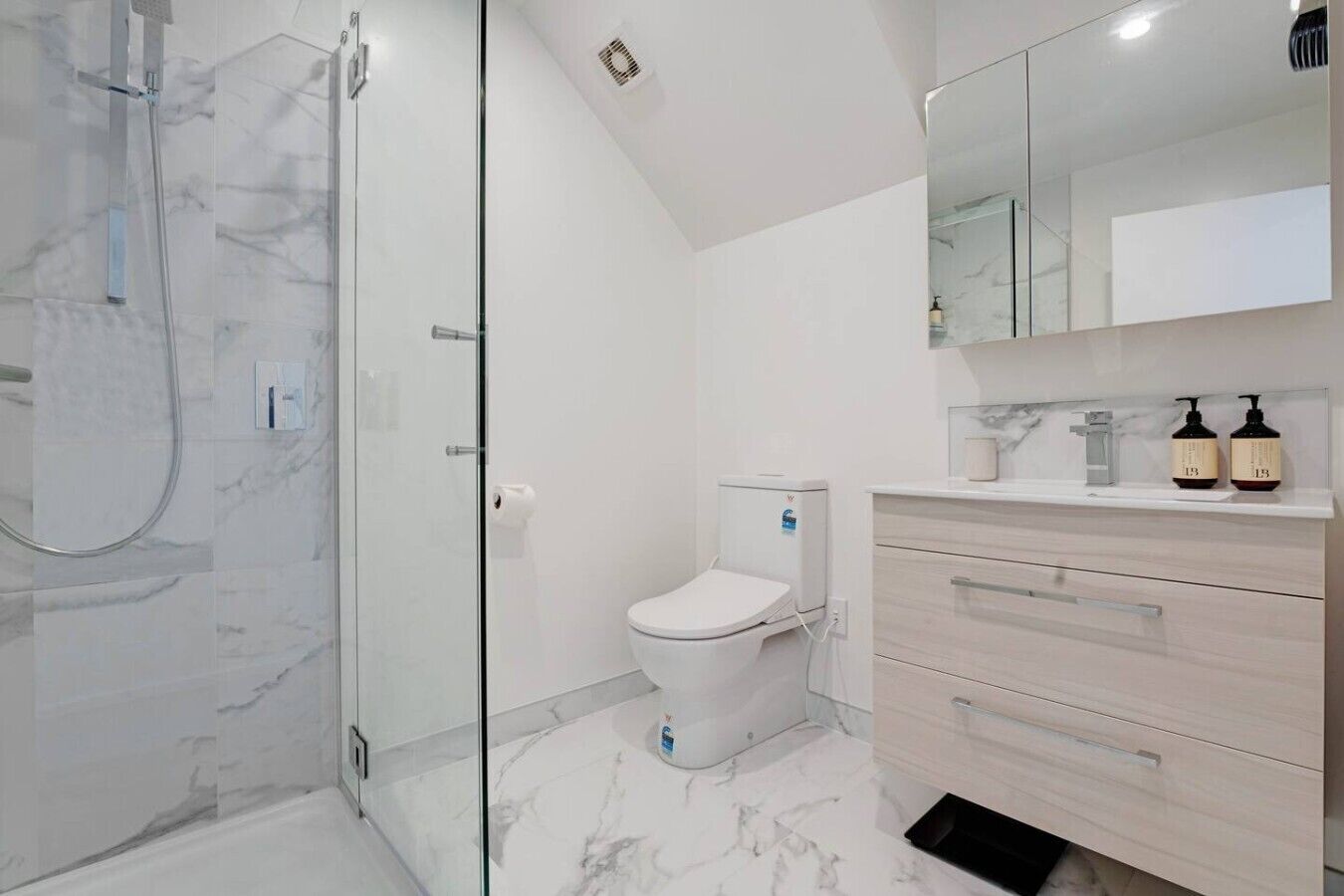 Une salle de bain moderne avec une douche à parois de verre, des toilettes blanches et un meuble-lavabo avec des tiroirs.