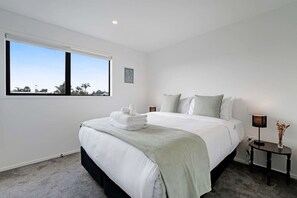 A modern hotel room with a large bed, a bedside table with a lamp, and a view through a window.
