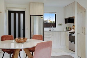 A modern kitchen with a dining area, featuring light wood cabinetry, a stainless steel refrigerator, and a white dining table with chairs.