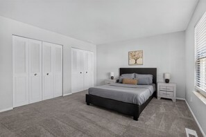 A bedroom with a bed, two bedside tables, a nightstand, a window with blinds, and a door with louvered shutters. - Spacious Townhome Designed for Relaxing Stays (Indianapolis)