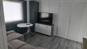 Un ambiente compatto con un divano, un piccolo tavolo rotondo, un televisore su un mobile e una porta.