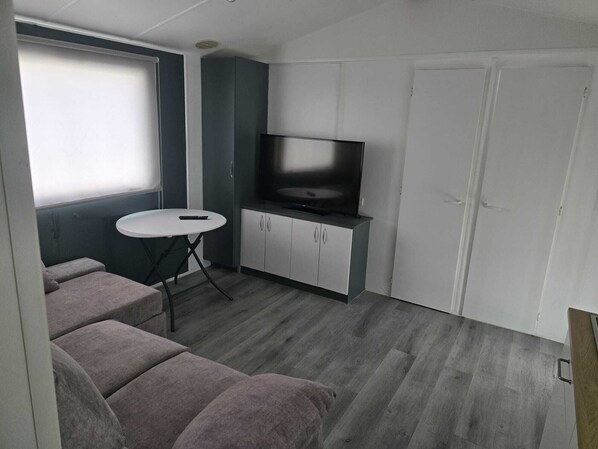 A compact living space with a sofa, a small round table, a television on a cabinet, and a door.