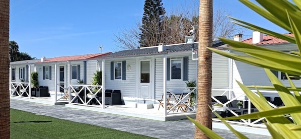 A row of white mobile homes with attached porches, each with a small table and chairs.