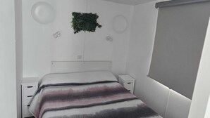 Una camera da letto con un letto, comodini, una pianta sospesa al muro e una finestra con tende.