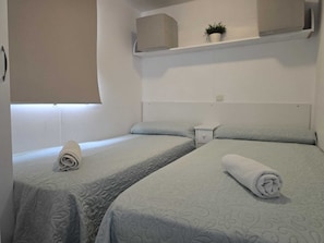 Habitación de hotel con dos camas individuales, una mesita de noche, una planta en maceta y una ventana con persiana.