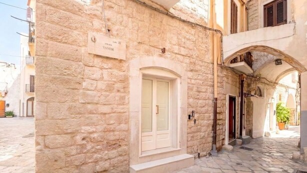 Un edificio de piedra con un letrero que indica 'Café 1X Strana Vaneze' y una puerta con un escalón pequeño que lleva a la entrada.