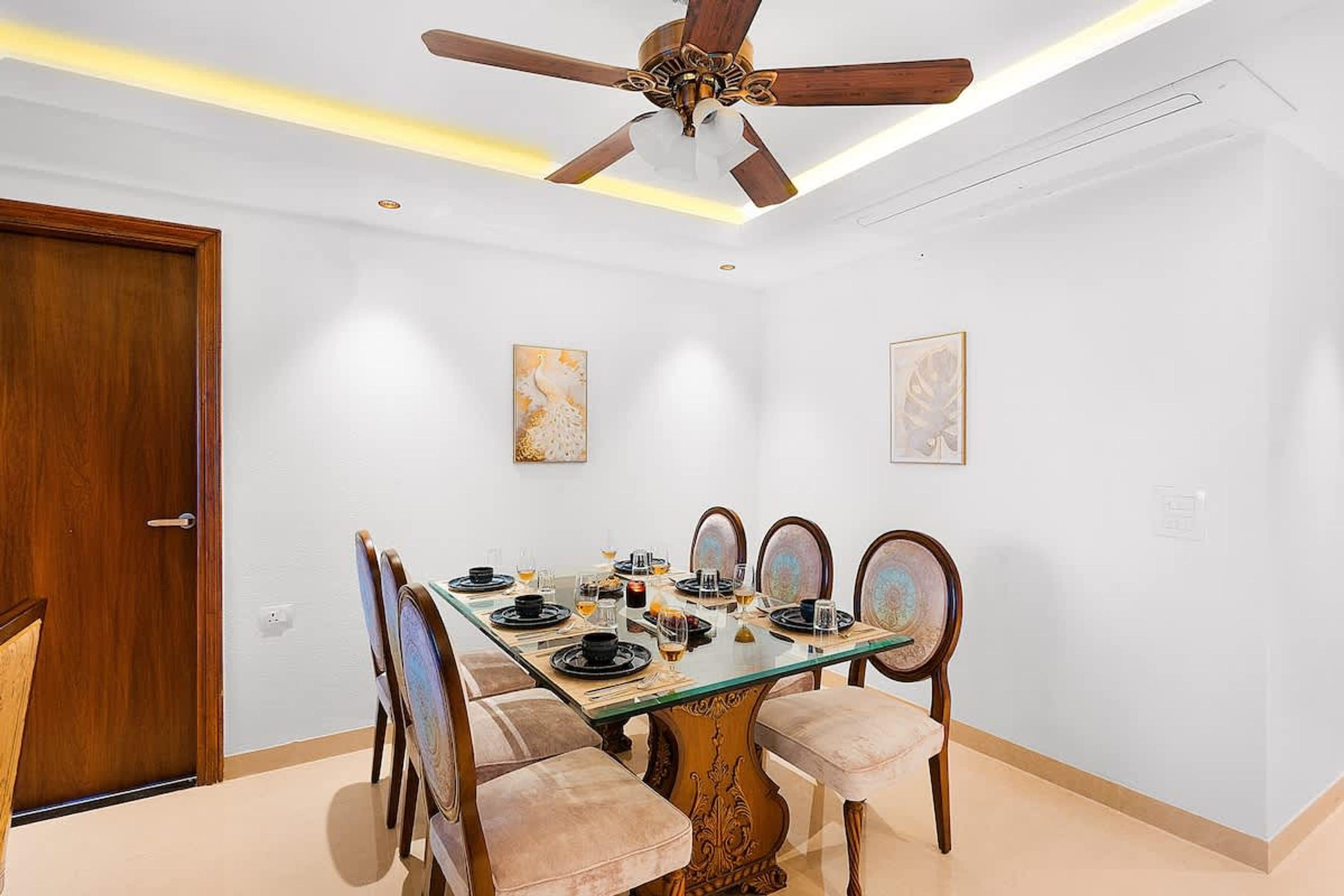 Comedor con mesa de vidrio, sillas de madera y un ventilador de techo.