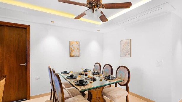 Un coin repas avec une table en verre, des chaises en bois et un ventilateur de plafond.