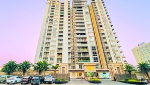 Un immeuble résidentiel de grande hauteur doté de nombreux balcons, d’une entrée sécurisée et d’un espace de stationnement avec des voitures.