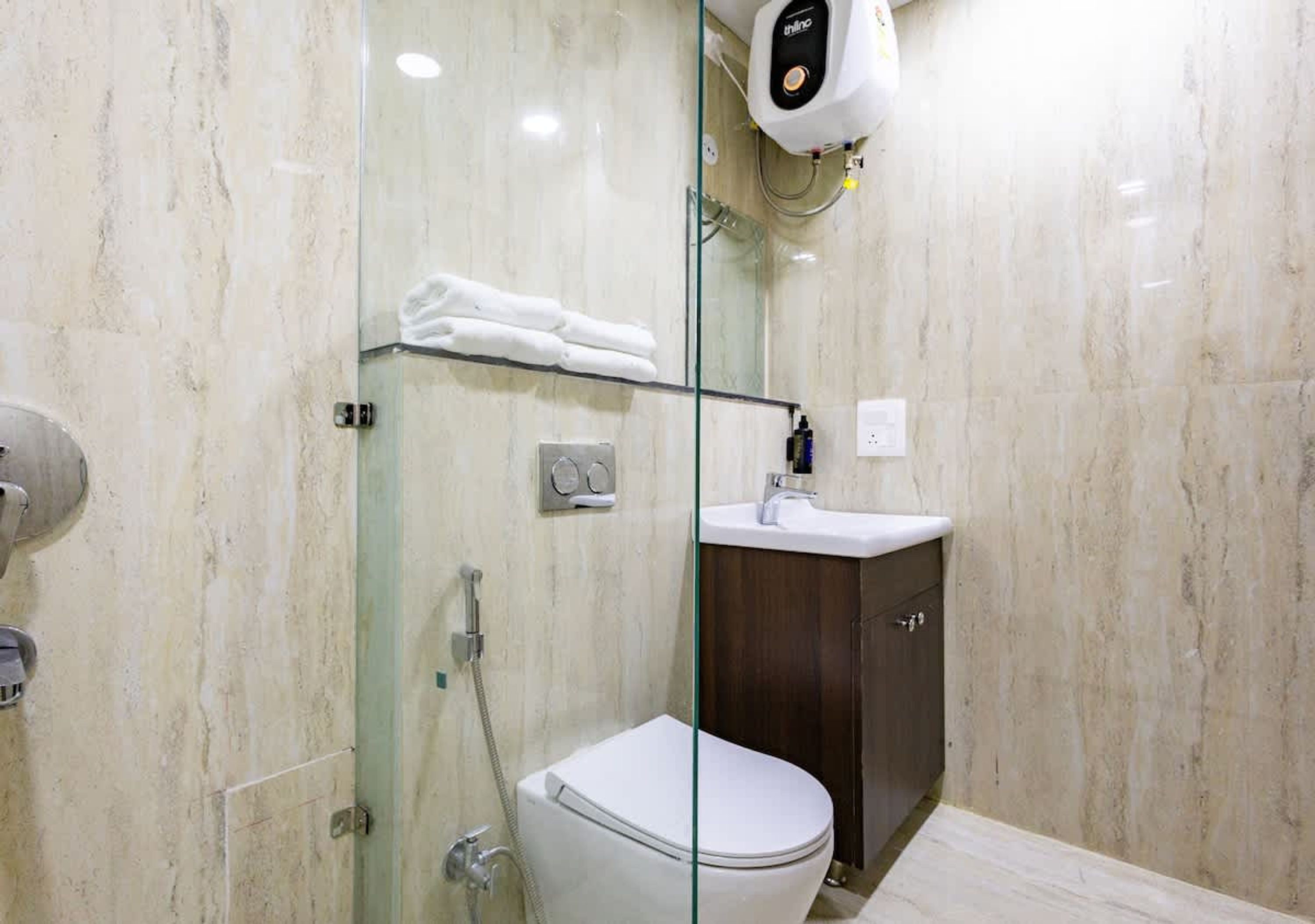 Een moderne badkamer met een douchecabine van glas, toilet, wastafel en een handdoekhouder.