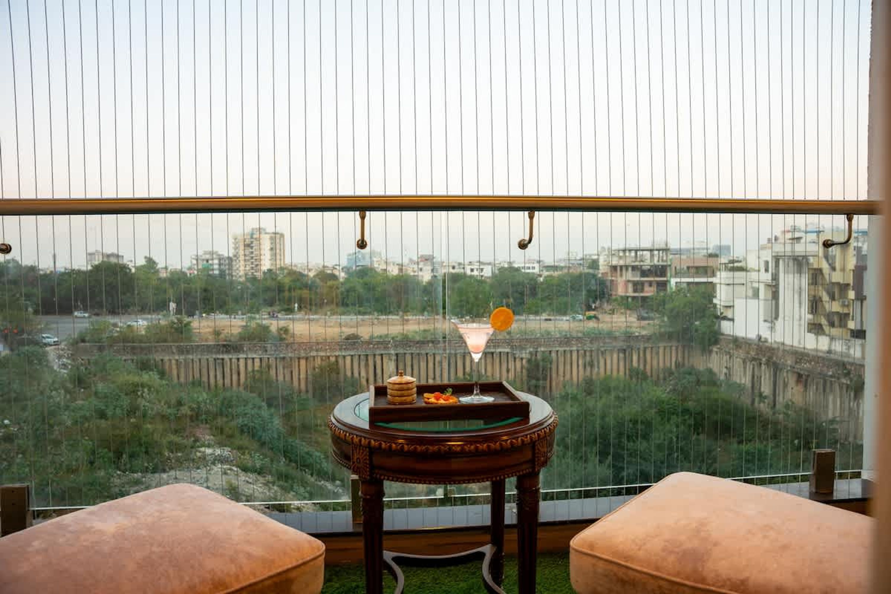 Un balcón con una mesa, dos asientos acolchados y vistas a un río y edificios.