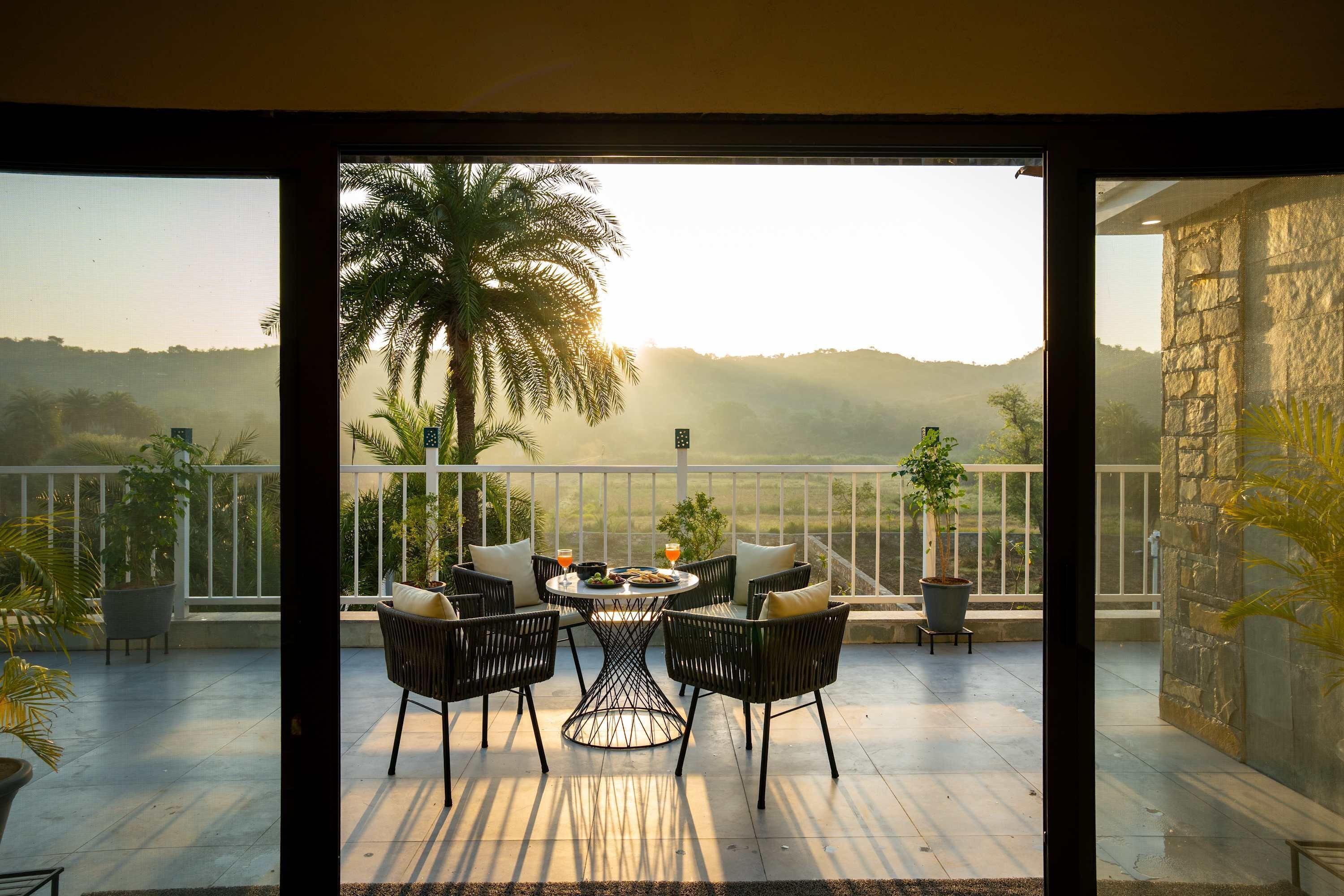 An outdoor patio with a table and chairs, overlooking a landscape with hills and palm trees.
