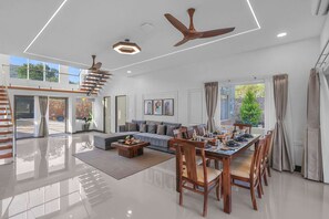 A spacious living area with a dining table set for six, a sofa, a staircase, and a ceiling fan.