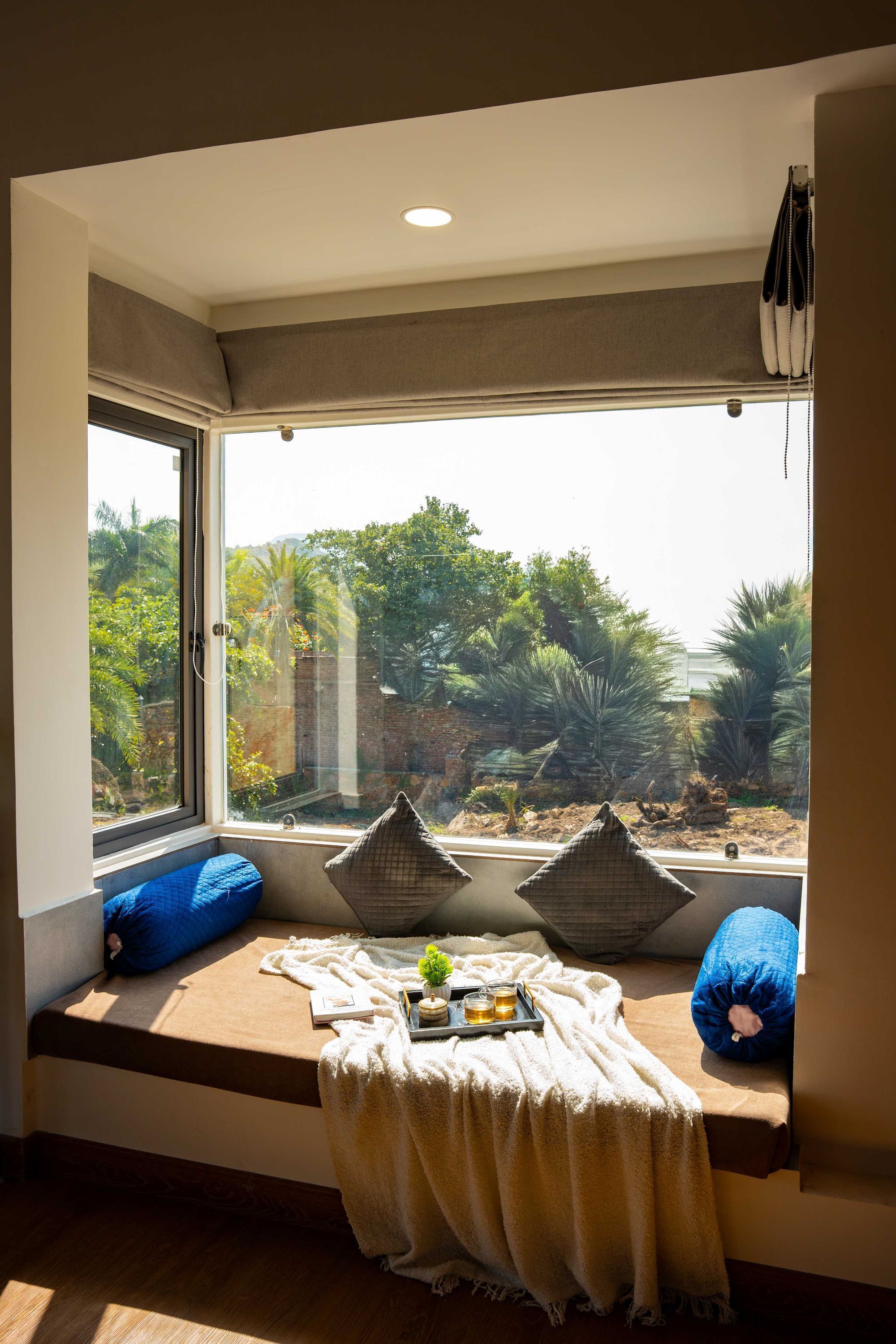 A room with a large window, a bench with cushions, a tray with drinks, and a small plant.