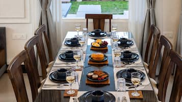 Mesa de jantar posta para seis, com pratos pretos, copos transparentes e diversas sobremesas.