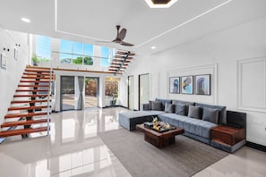 Un amplio salón con una escalera moderna, un sofá modular y una mesa de centro.