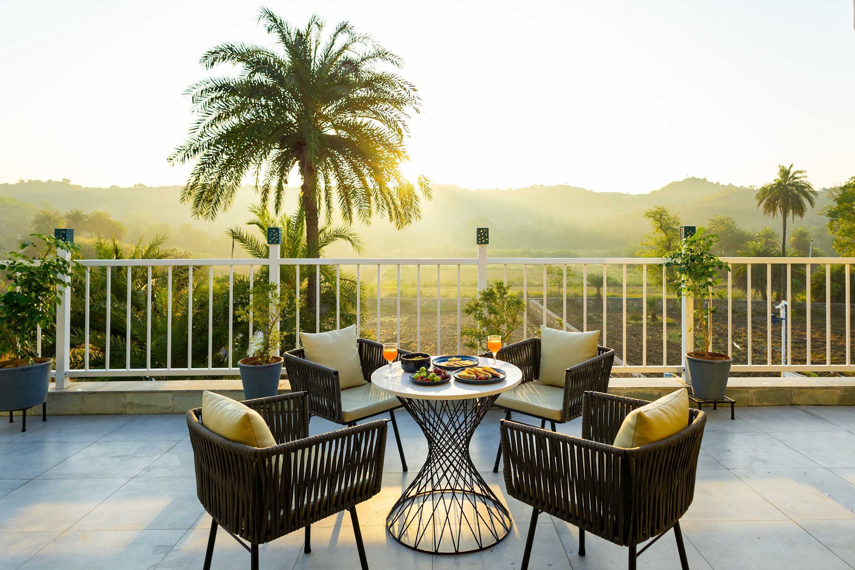 A terrace with wicker furniture, a round table, and a view of palm trees and hills.