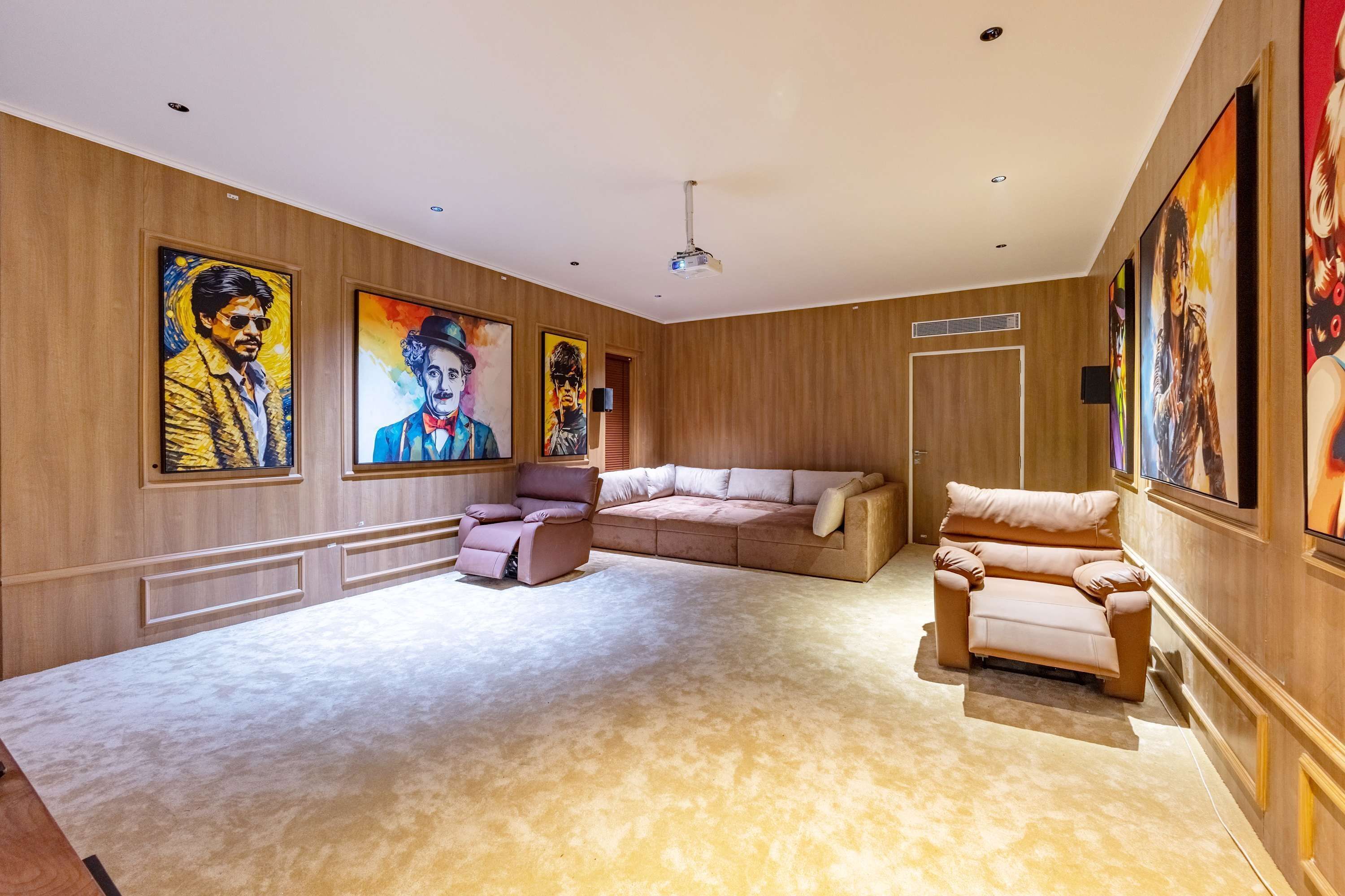 A spacious living room with a large sectional sofa, a recliner, and a coffee table. The walls are adorned with large, colorful paintings.