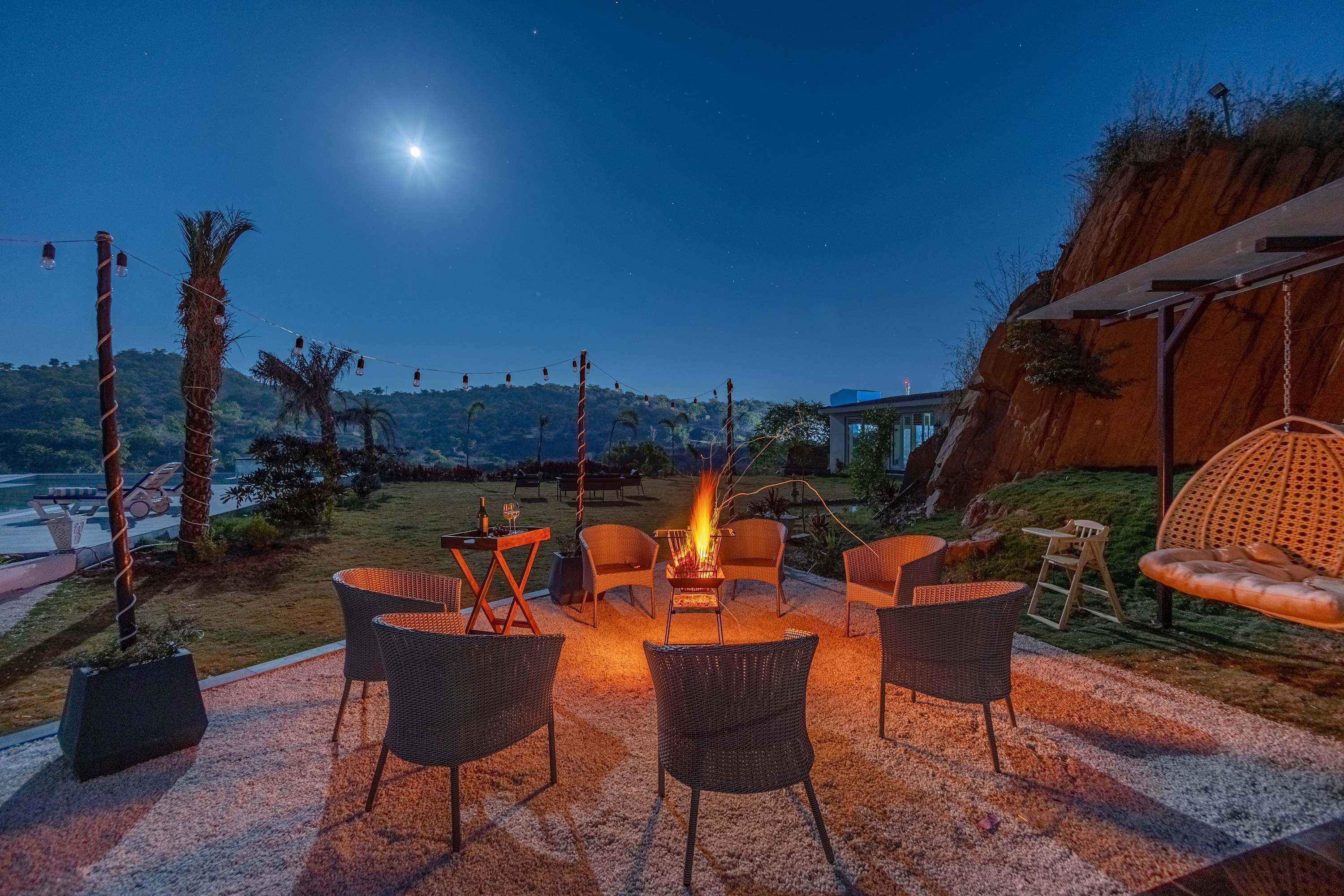 An outdoor seating area with wicker chairs and a fire pit, overlooking a scenic landscape with a clear night sky and distant hills.