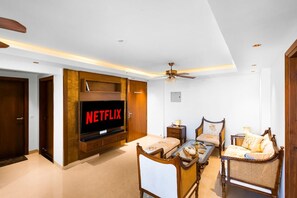 A modern living room with a television displaying 'NETFLIX,' a ceiling fan, and traditional furniture. - The Majestic Crown - 2bhk Luxury Home by Viraalay (Jaipur)