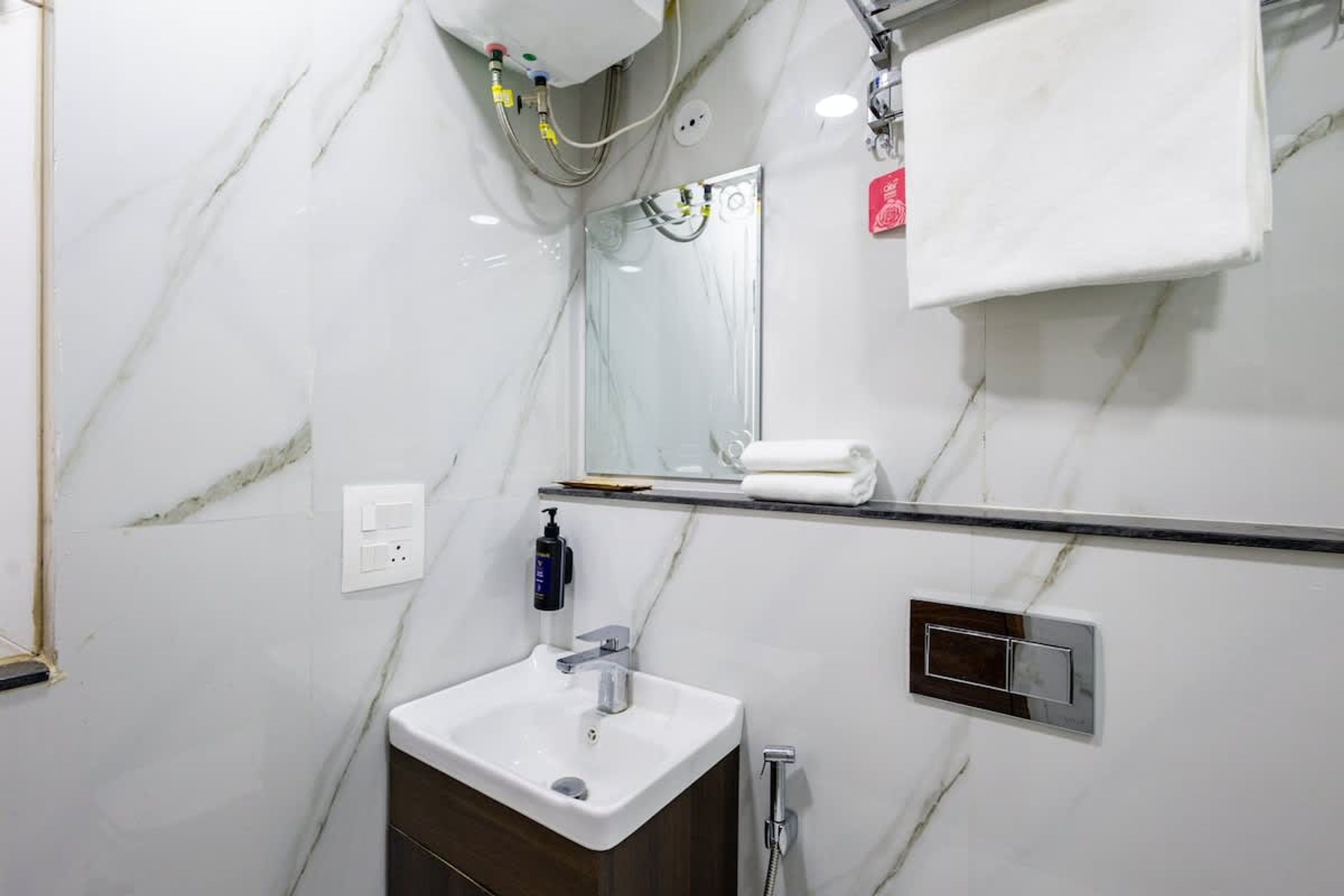 Un baño con pared de mármol, lavamanos, espejo, toallero y ducha.