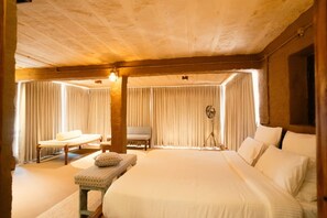 A room with a large bed, a small table, a chair, and a floor lamp.