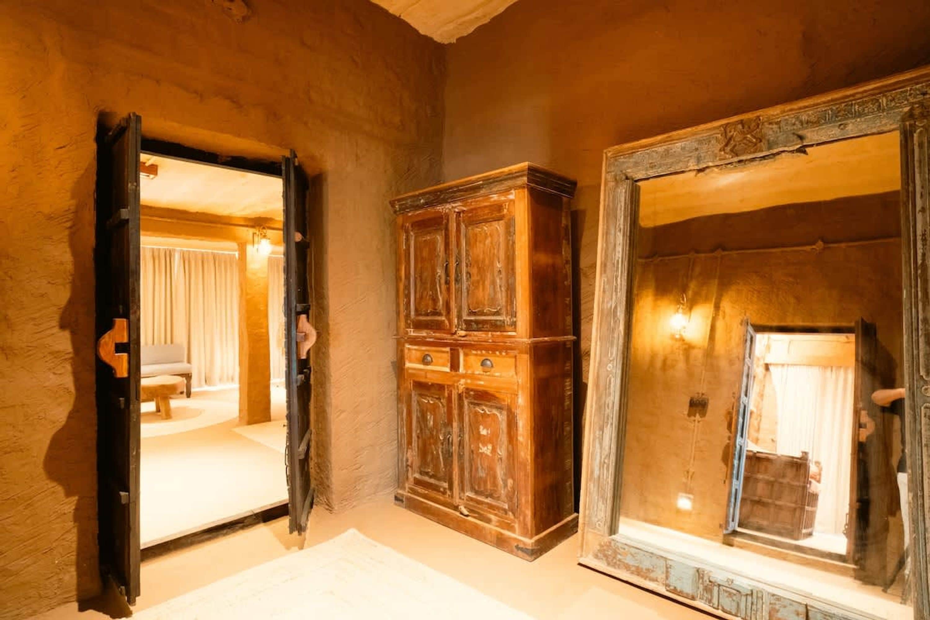 Ein Zimmer mit einem Holzkabinett und einem Spiegel mit dekorativem Rahmen.