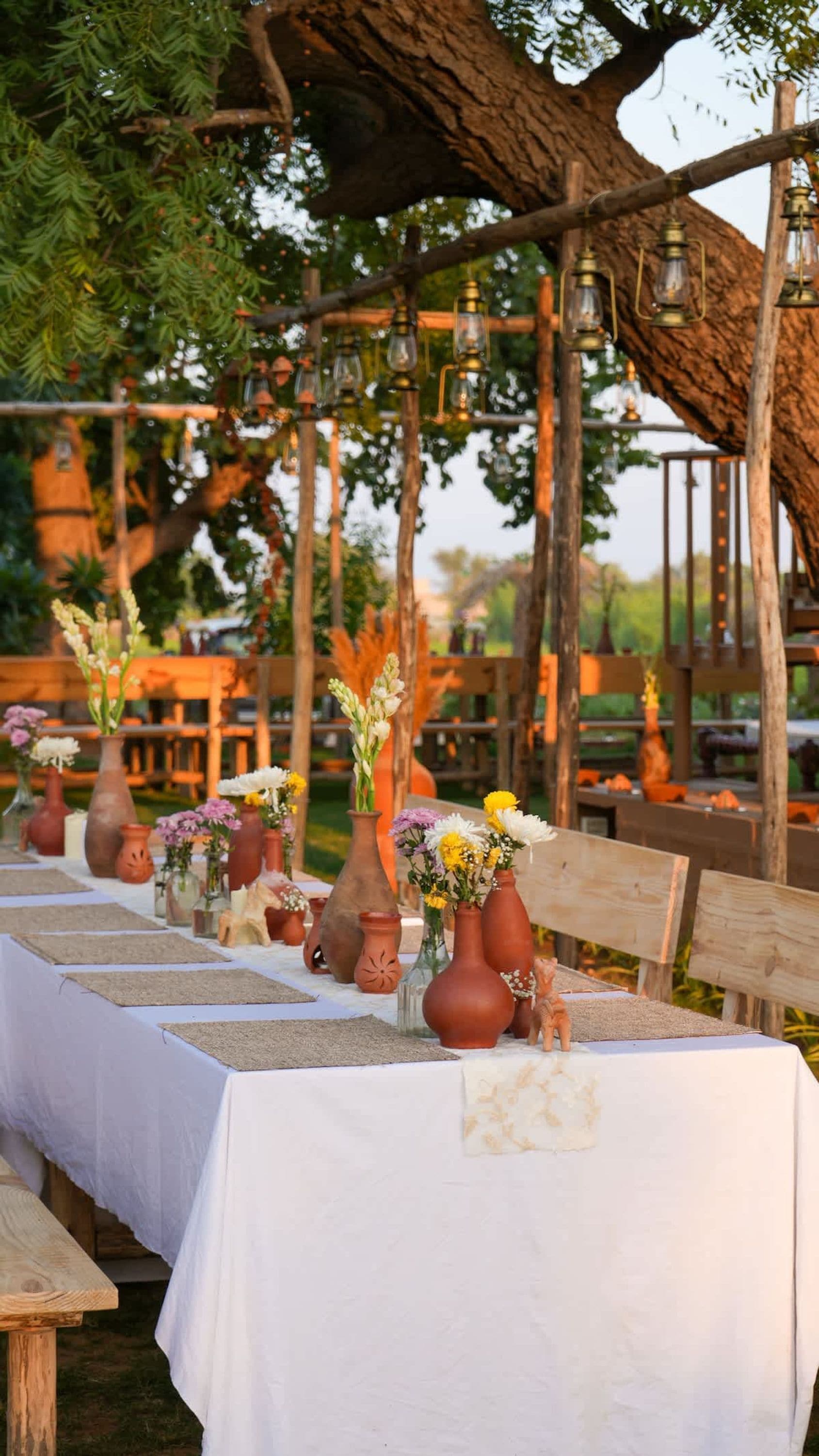 Un espace de restauration en plein air avec des bancs et des tables en bois rustique, recouverts de nappes blanches.