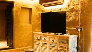 Una stanza con una televisione su un mobile in legno, una porta e un muro in pietra.