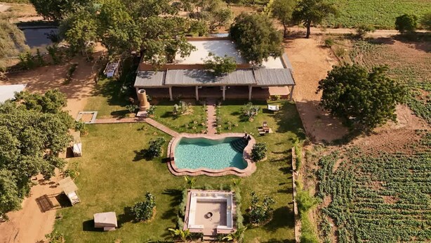 A large building with a swimming pool, surrounded by a well-maintained lawn and a vineyard.
