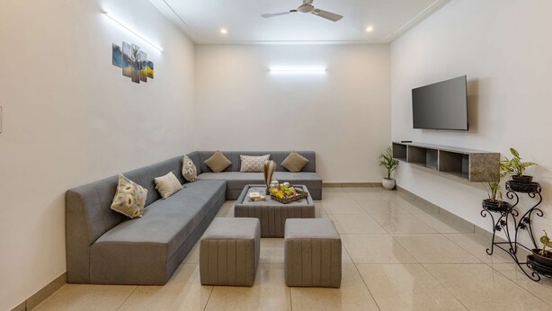 A modern living room with a grey sectional sofa, a flat-screen TV mounted on the wall, and a ceiling fan.