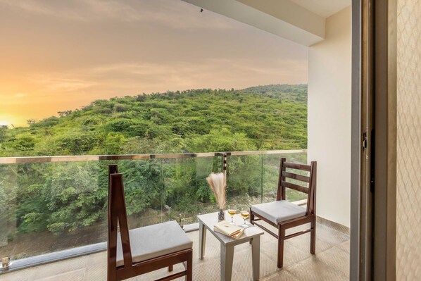 A balcony with two wooden chairs and a small table, overlooking a lush green landscape.