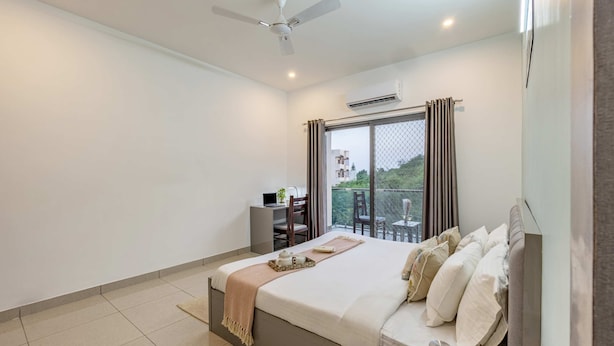 A hotel room with a bed, a desk with a laptop, a chair, and a view of the outside.