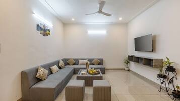 A modern living room with a grey sectional sofa, a flat-screen TV mounted on the wall, and a ceiling fan.